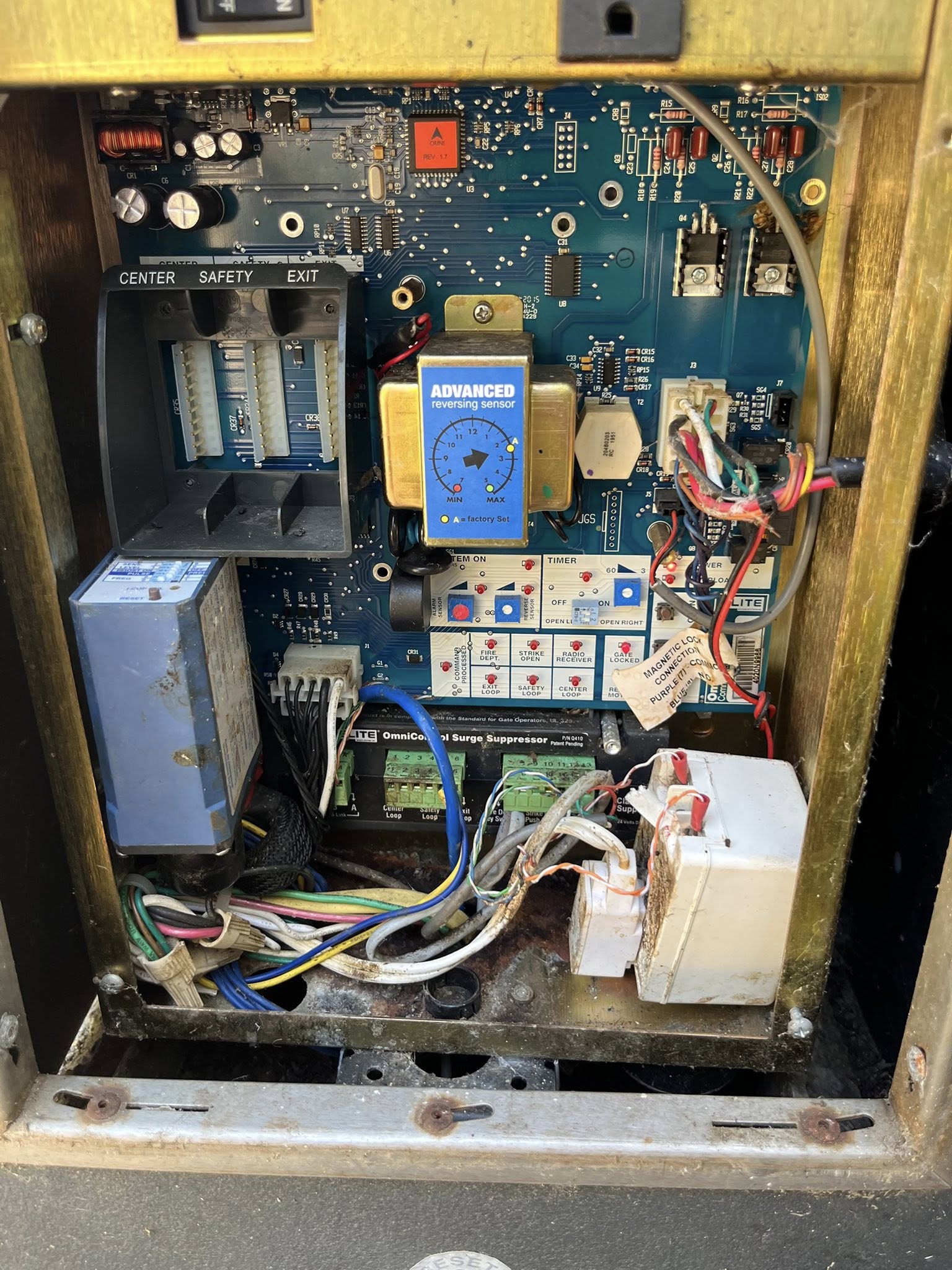 Open control panel with visible circuit board, various wires, fuses, a blue transformer, labeled switches, and electronic components arranged inside a metal enclosure.